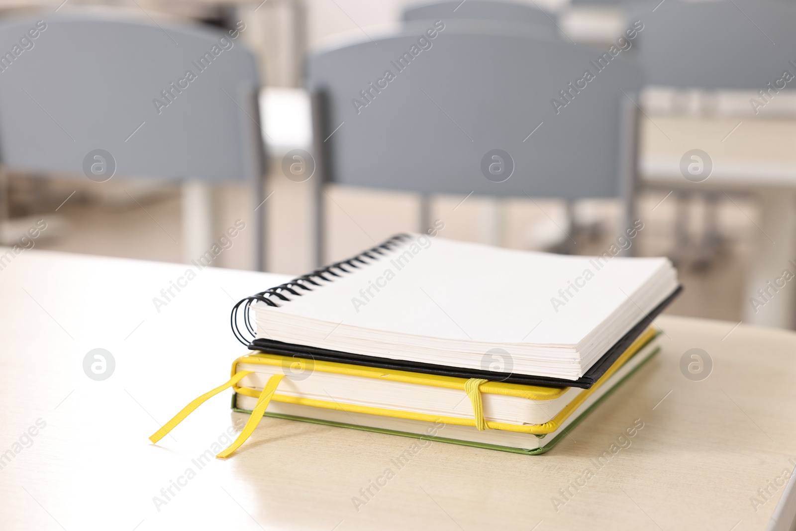 Photo of Stack of notebooks on wooden desk in empty classroom