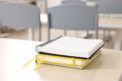 Stack of notebooks on wooden desk in empty classroom