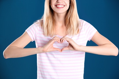 Woman making heart with her hands on color background, closeup