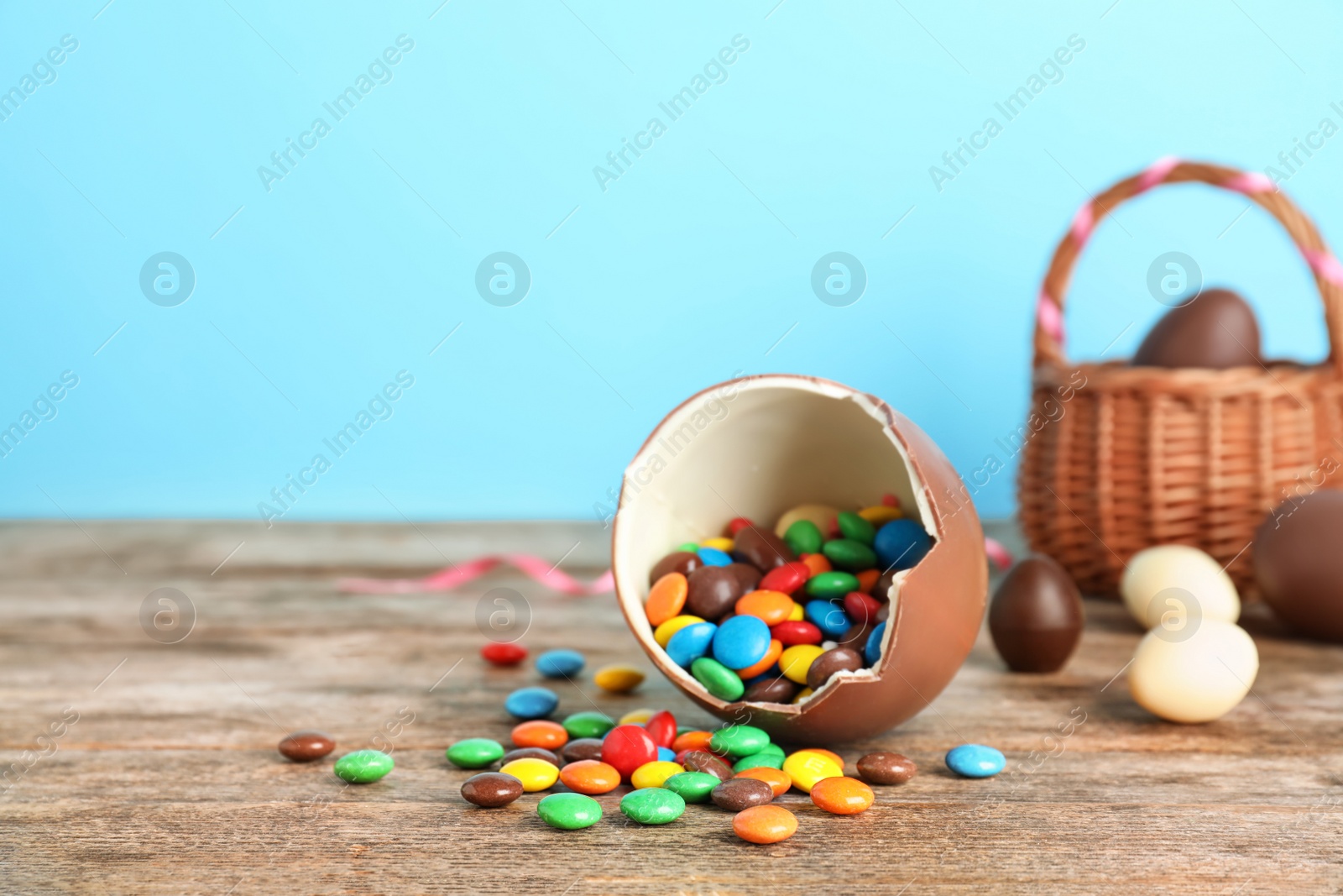 Photo of Broken chocolate Easter egg with candies on wooden table. Space for text