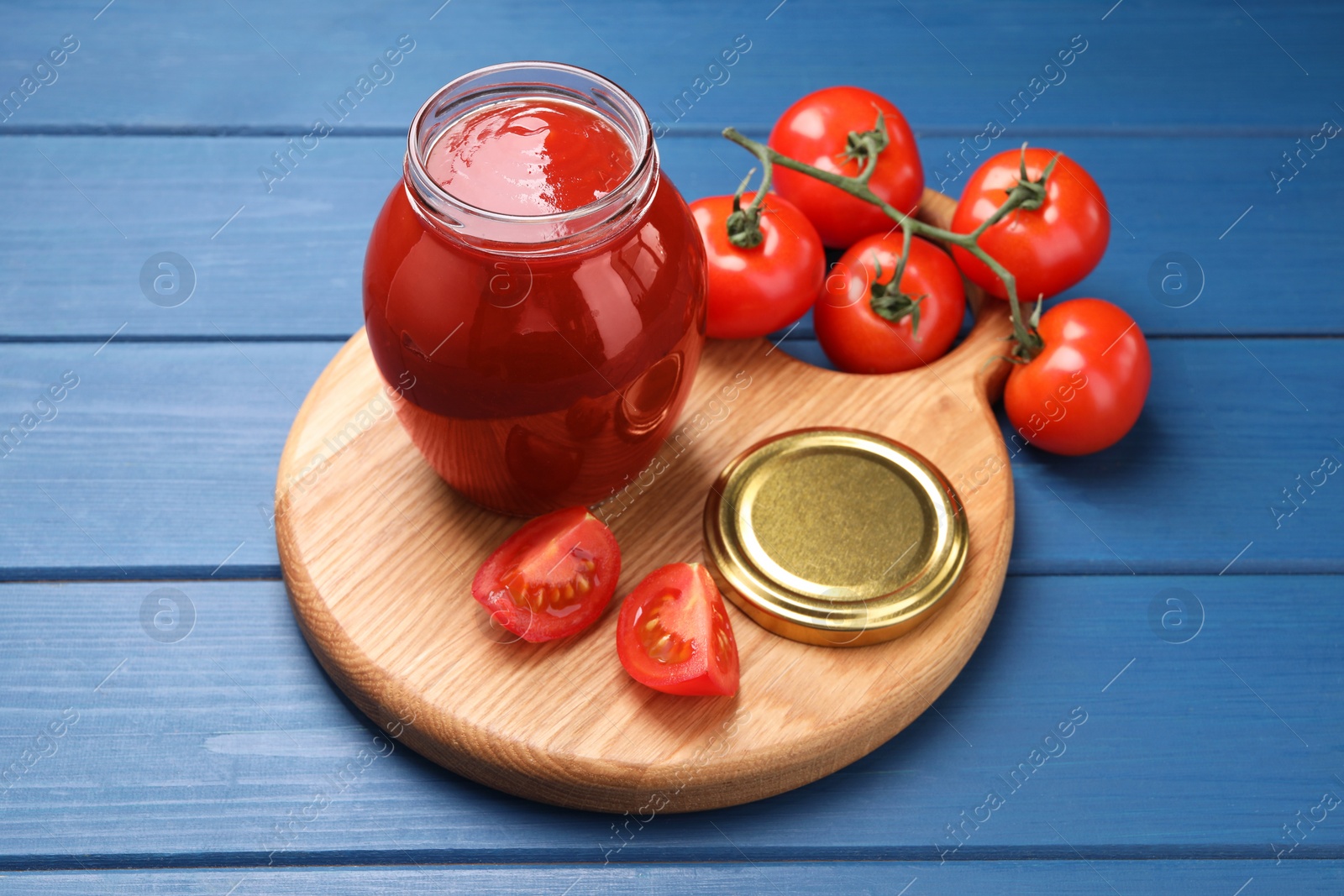 Photo of Organic ketchup in jar and fresh tomatoes on blue wooden table. Tomato sauce