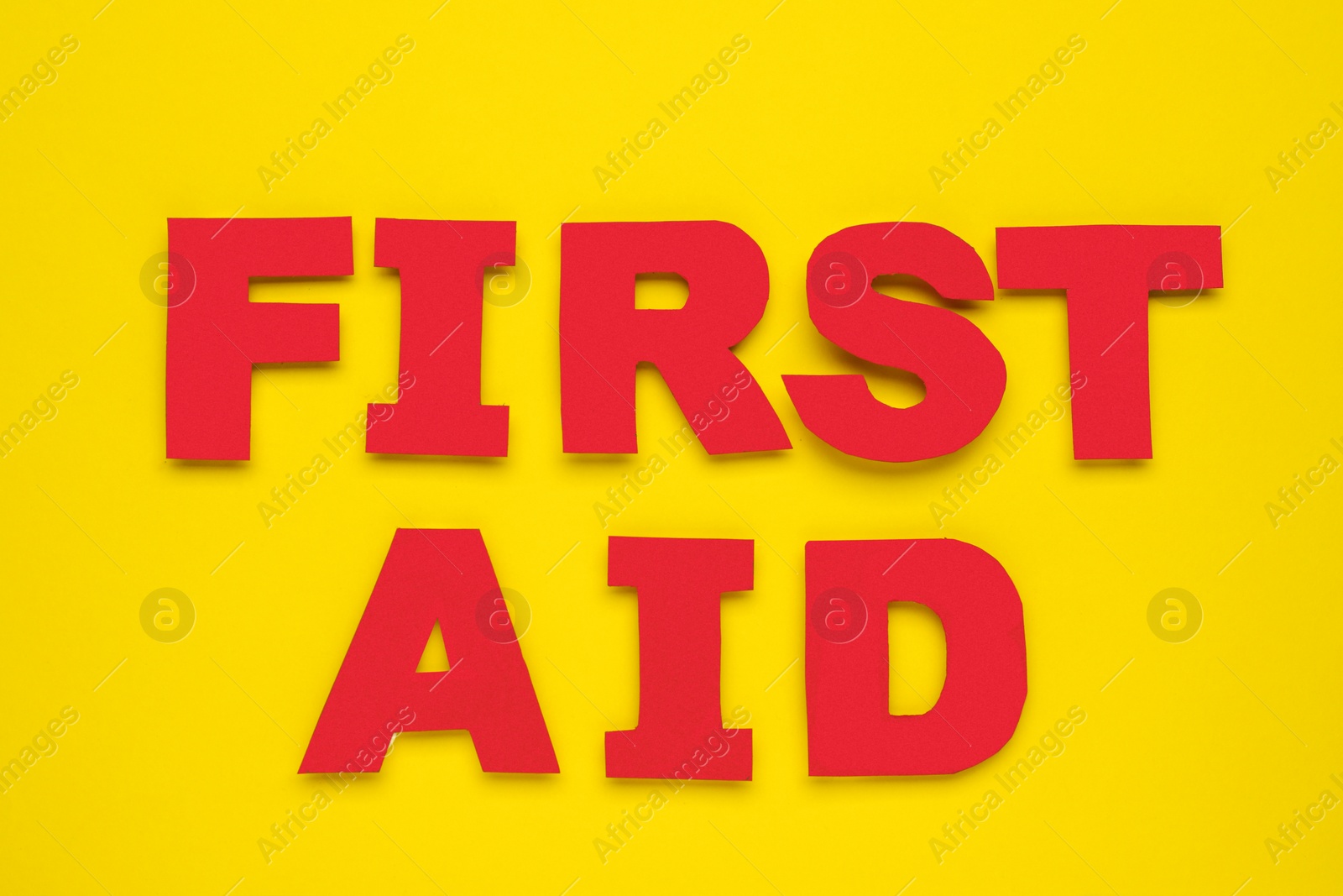 Photo of Words First Aid made of red letters on yellow background, flat lay
