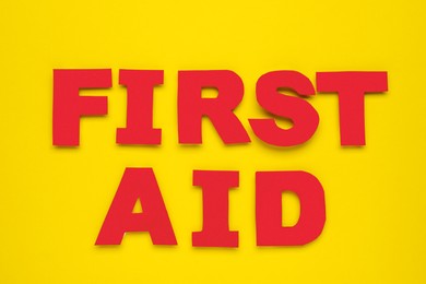 Words First Aid made of red letters on yellow background, flat lay