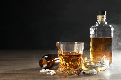 Photo of Alcohol and drug addiction. Whiskey in glass, syringe, pills and cigarettes on wooden table, space for text