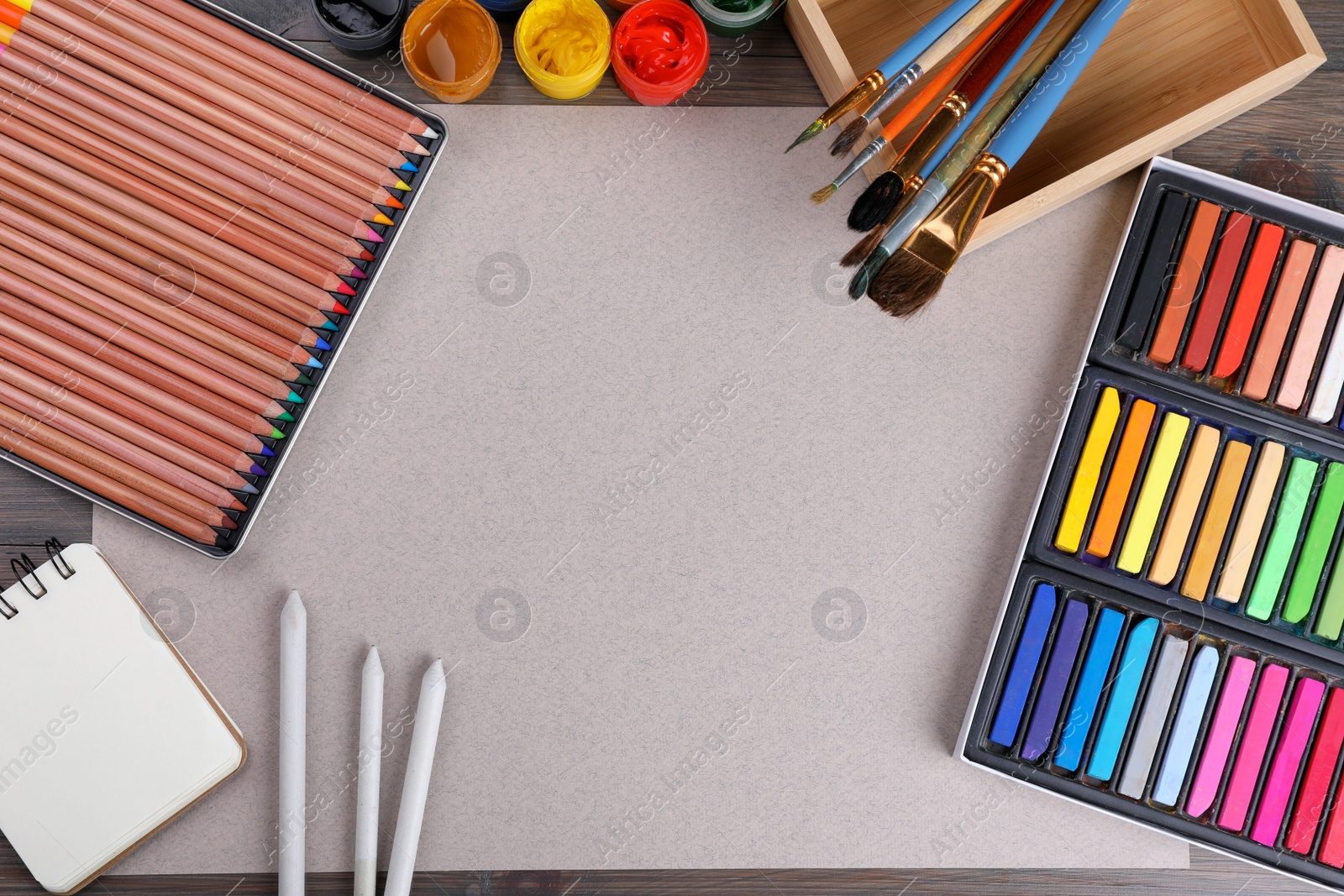 Photo of Blank sheet of paper, colorful chalk pastels and other drawing tools on wooden table, flat lay. Modern artist's workplace