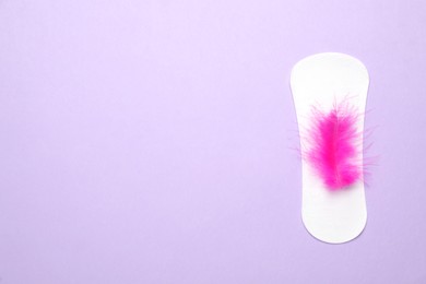 Sanitary pad with pink feather on violet background, top view and space for text. Menstrual cycle