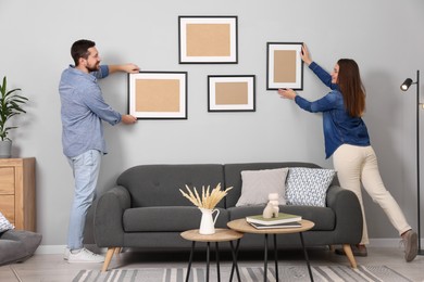 Photo of Man and woman hanging picture frames on gray wall at home