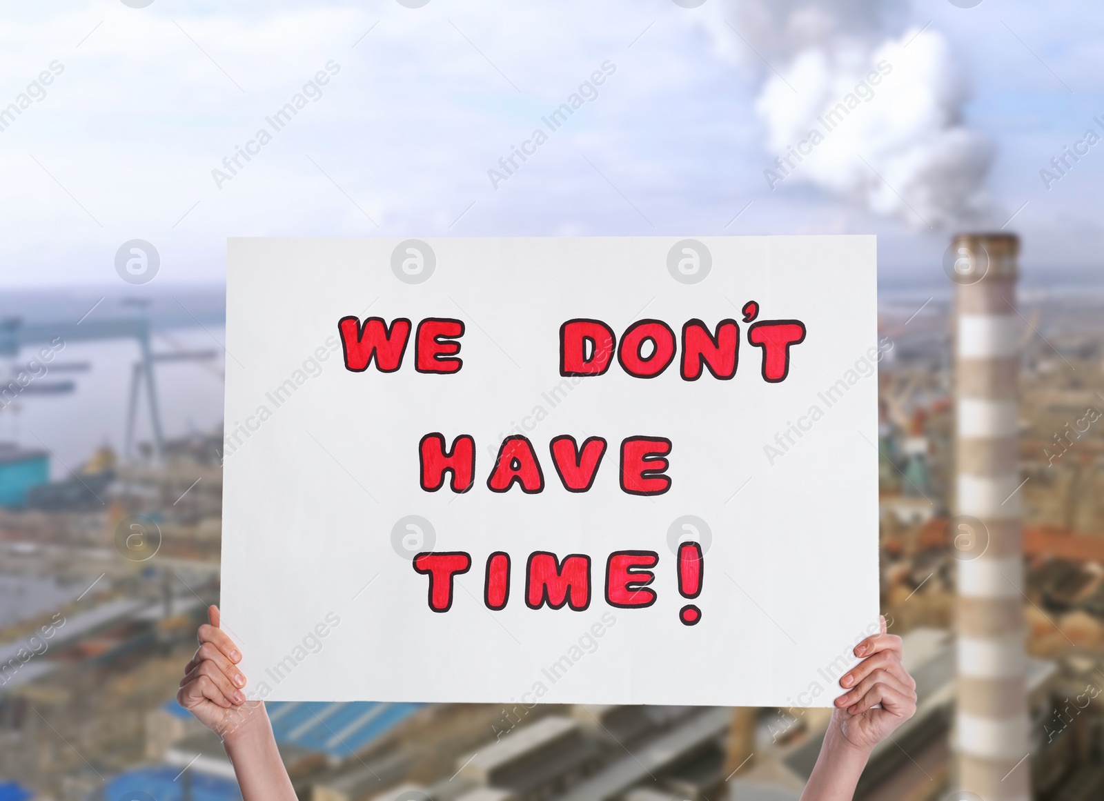 Image of Protestor holding placard with text We Don't Have Time and blurred view of industrial factory on background. Climate strike