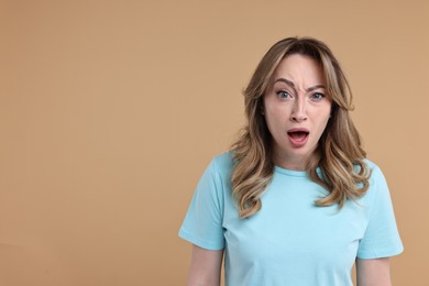 Portrait of surprised woman on beige background. Space for text