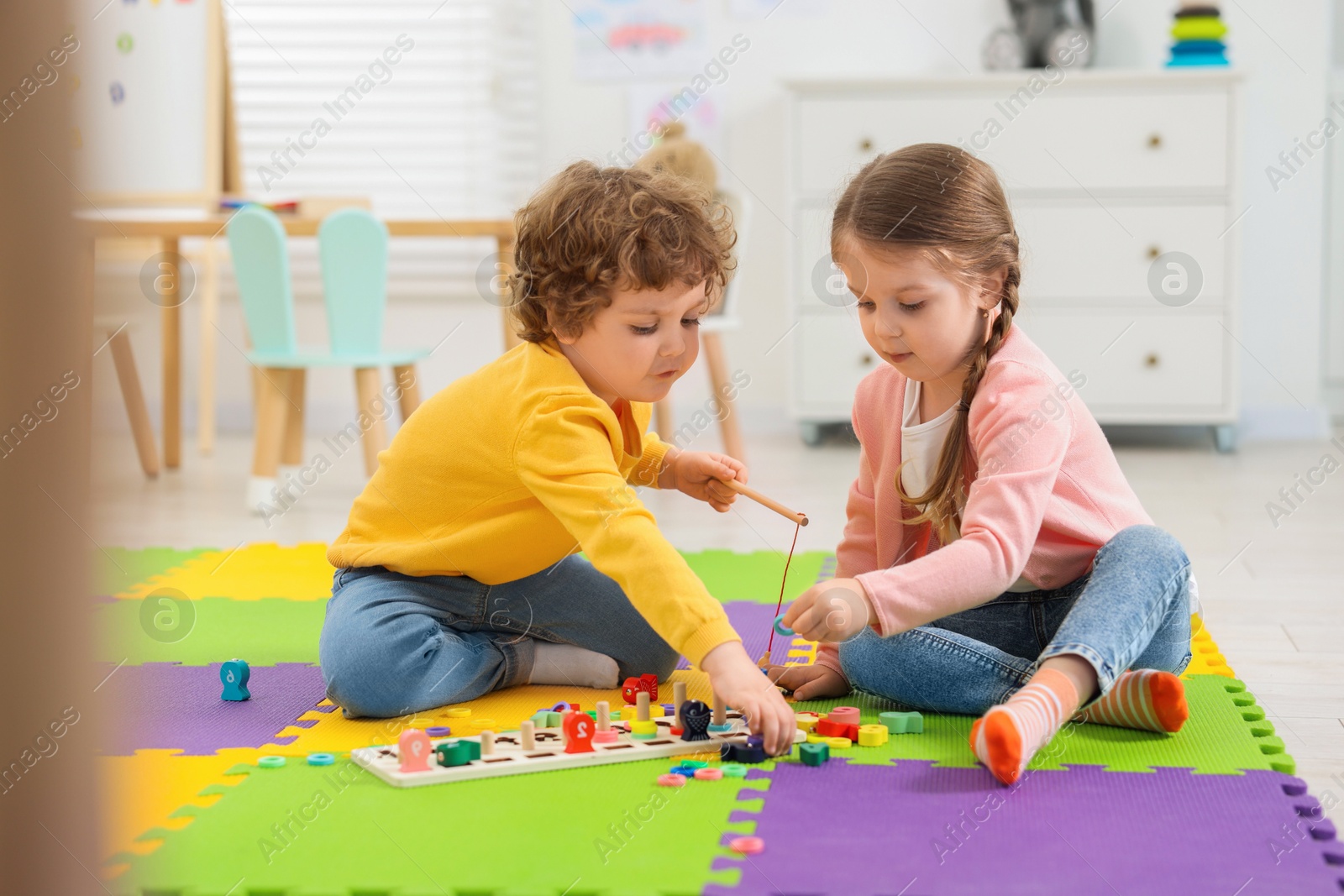 Photo of Cute little children playing with math game Fishing for Numbers on puzzle mat in kindergarten