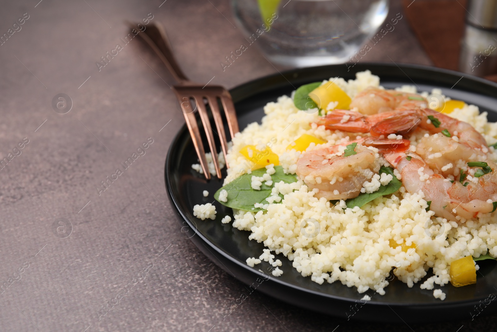 Photo of Tasty couscous with shrimps, bell pepper and basil on brown textured table, closeup. Space for text