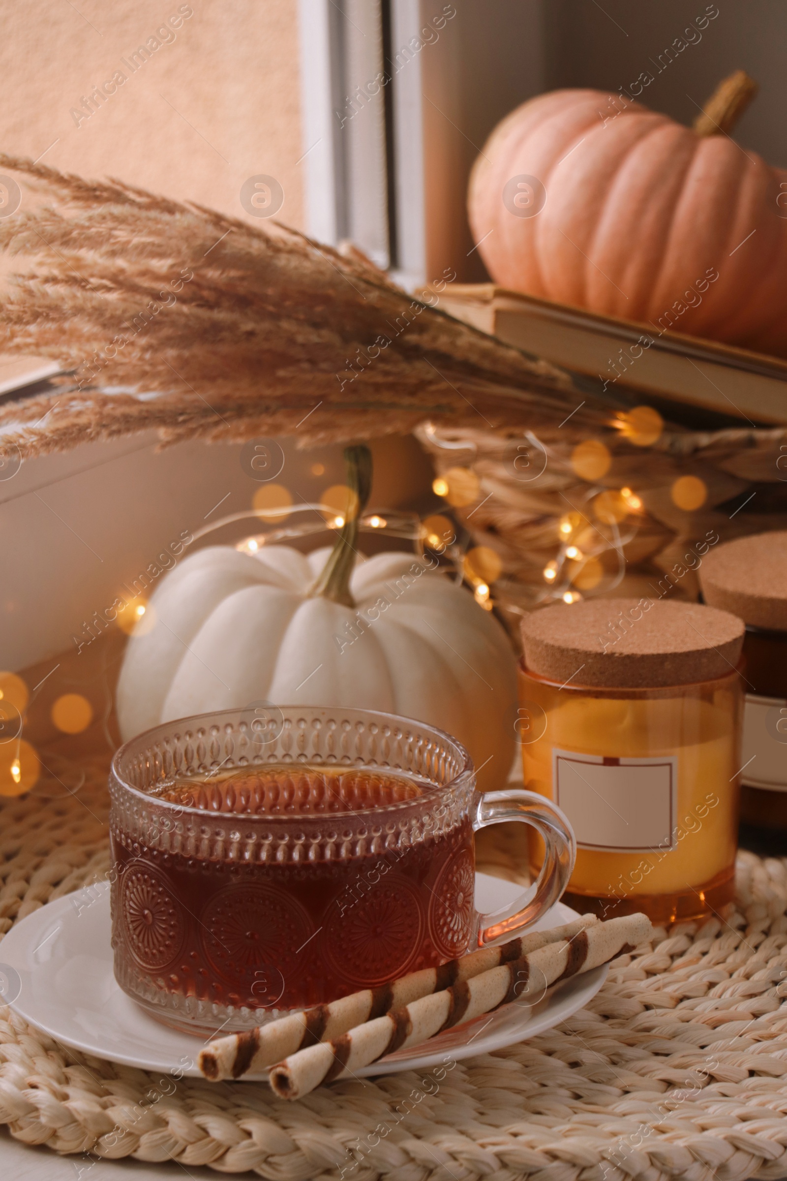 Photo of Cup of hot drink, cookies, candles and pumpkins on window sill indoors