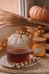 Cup of hot drink, cookies, candles and pumpkins on window sill indoors