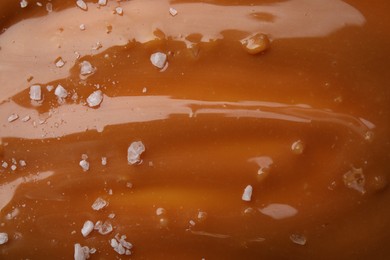 Photo of Delicious caramel sauce with sea salt as background, closeup