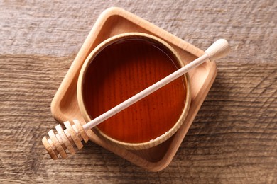 Photo of Delicious honey in bowl and dipper on wooden table, top view