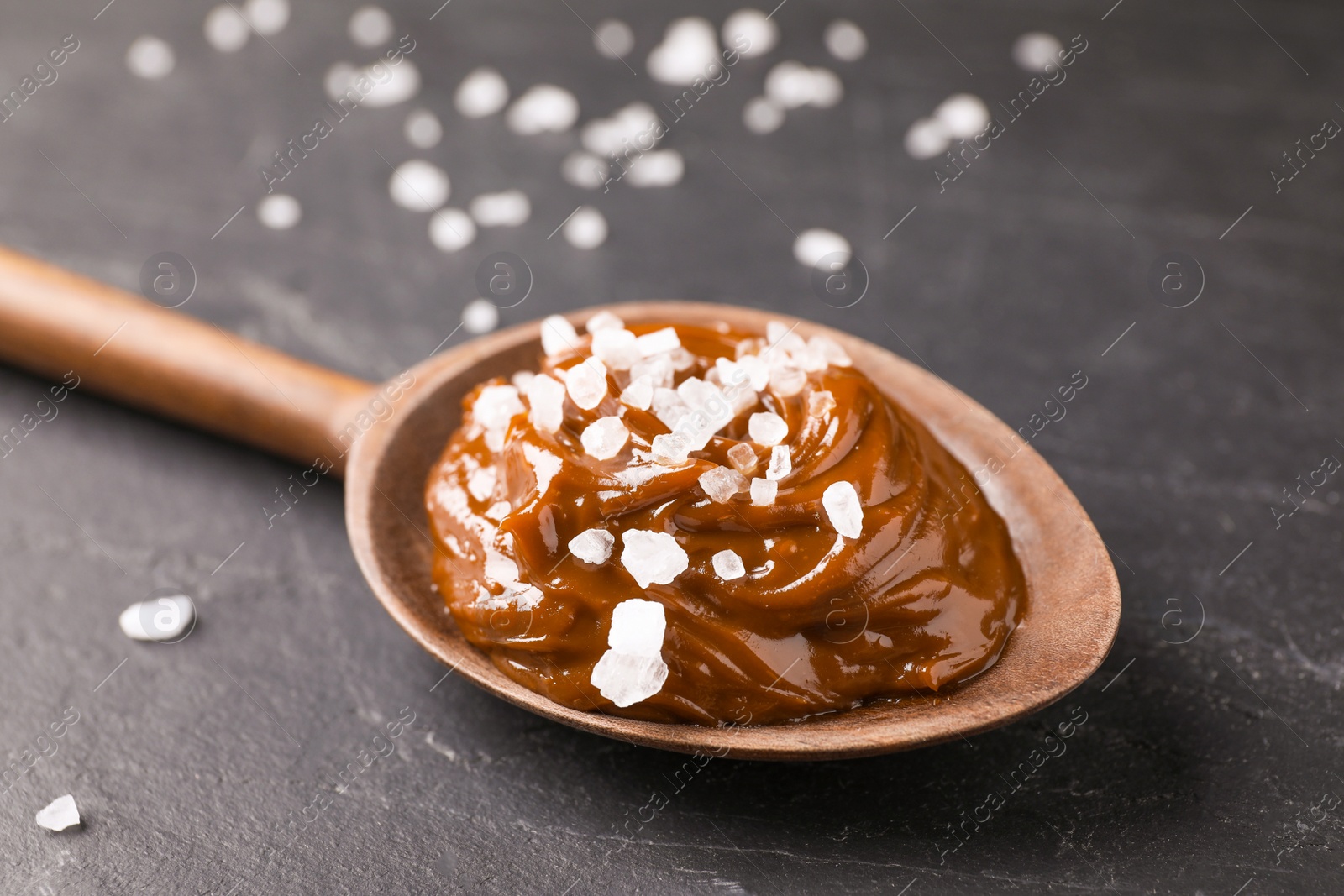 Photo of Salted caramel in spoon on grey table, closeup