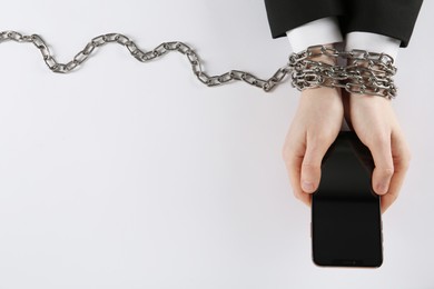 Photo of Man with chained hands holding smartphone on white background, top view. Internet addiction