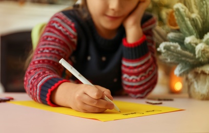 Photo of Cute child writing letter to Santa Claus at table, closeup. Christmas tradition