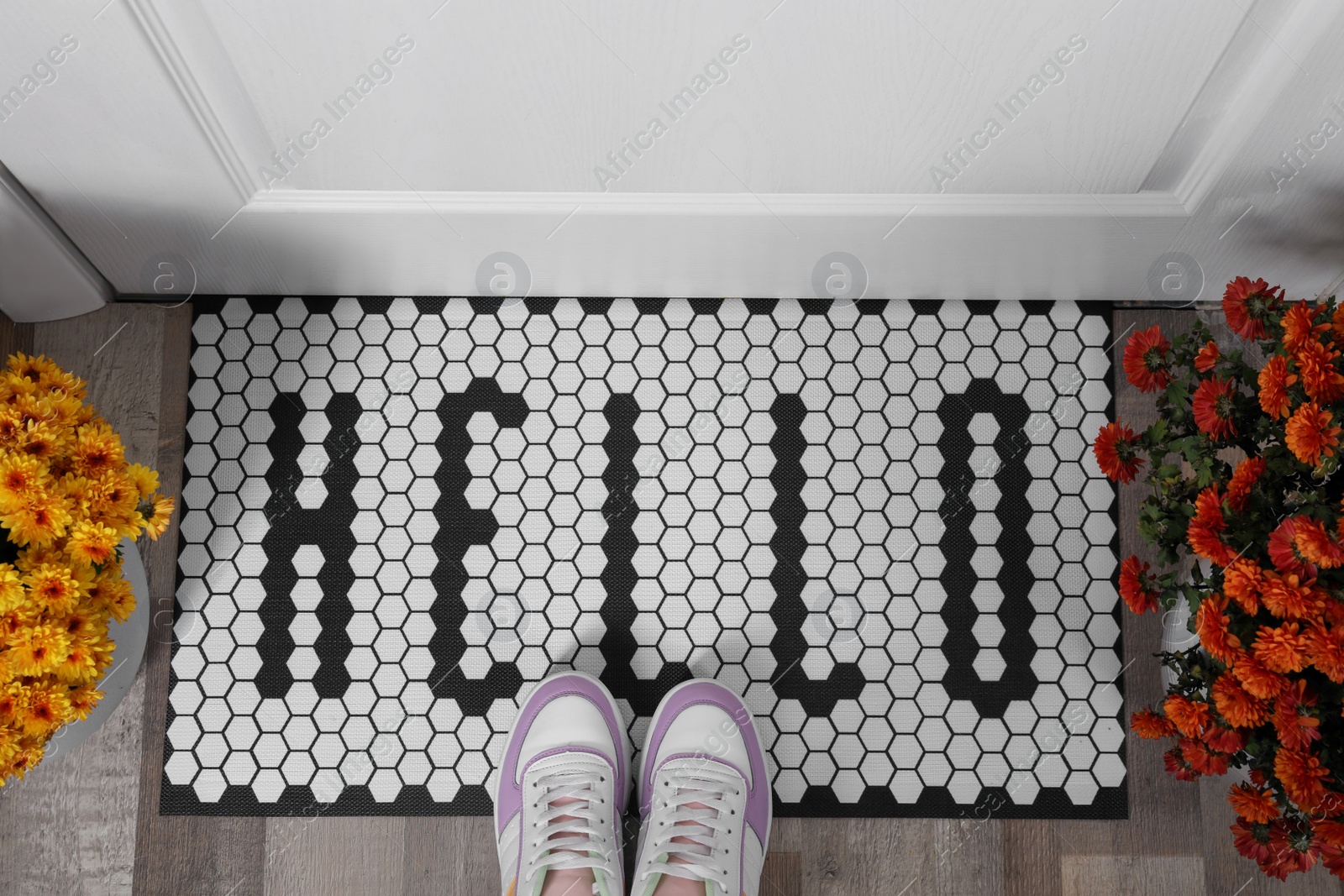 Photo of Stylish door mat with word Hello, beautiful flowers and shoes on floor, flat lay