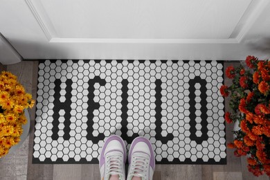 Stylish door mat with word Hello, beautiful flowers and shoes on floor, flat lay