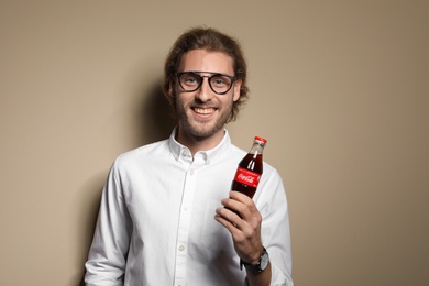 Photo of MYKOLAIV, UKRAINE - NOVEMBER 28, 2018: Young man with bottle of Coca-Cola on color background