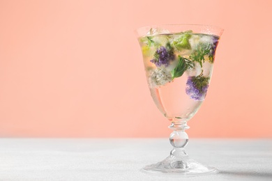 Glass of ice cubes with flowers on light table against pink background. Space for text