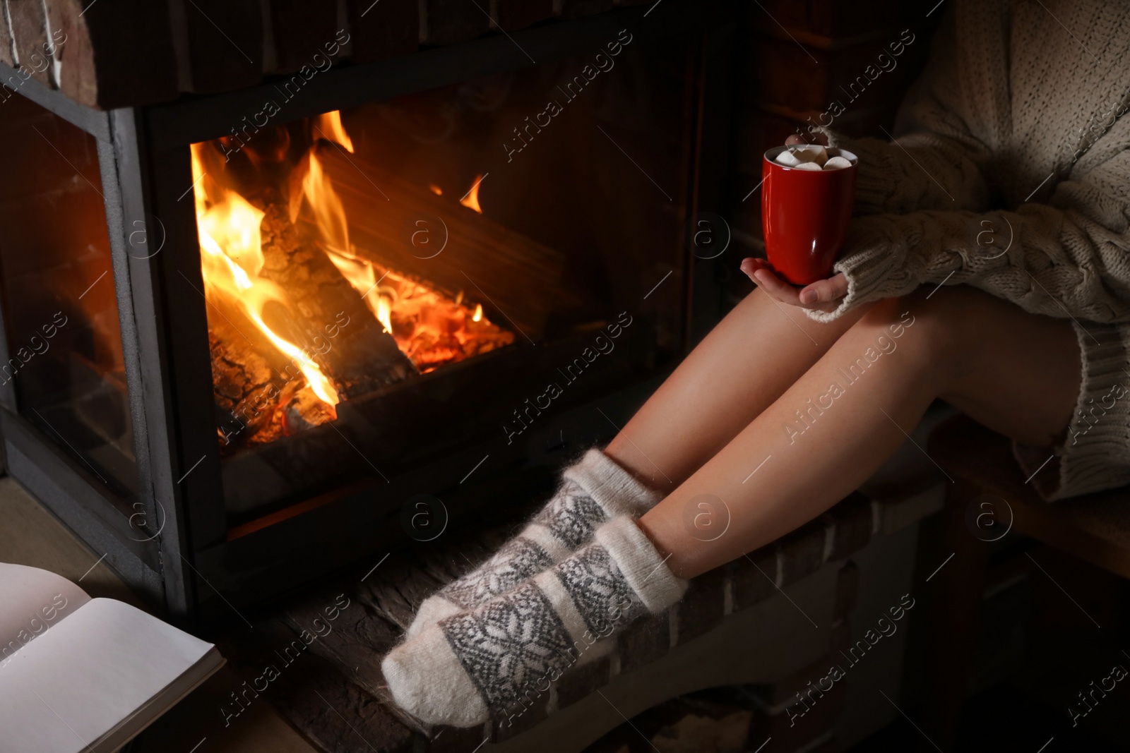 Photo of Woman with cup of delicious cocoa resting near fireplace at home, closeup. Winter vacation