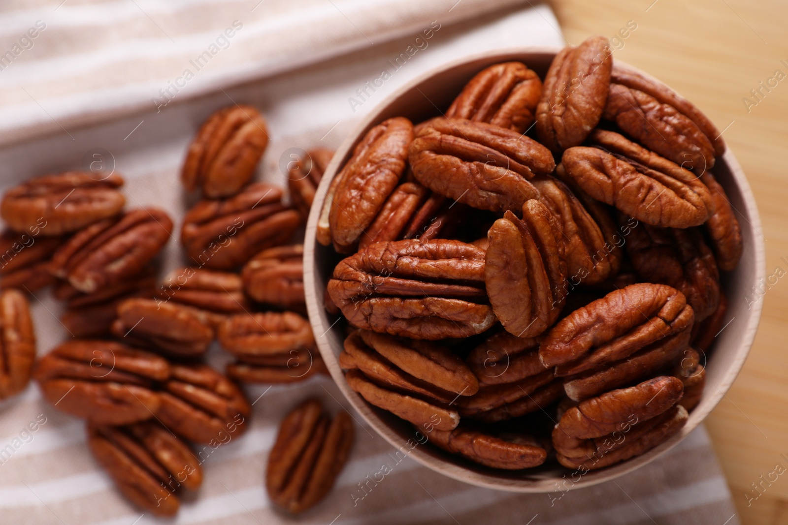 Photo of Tasty pecan nuts with bowl and cloth on table, flat lay