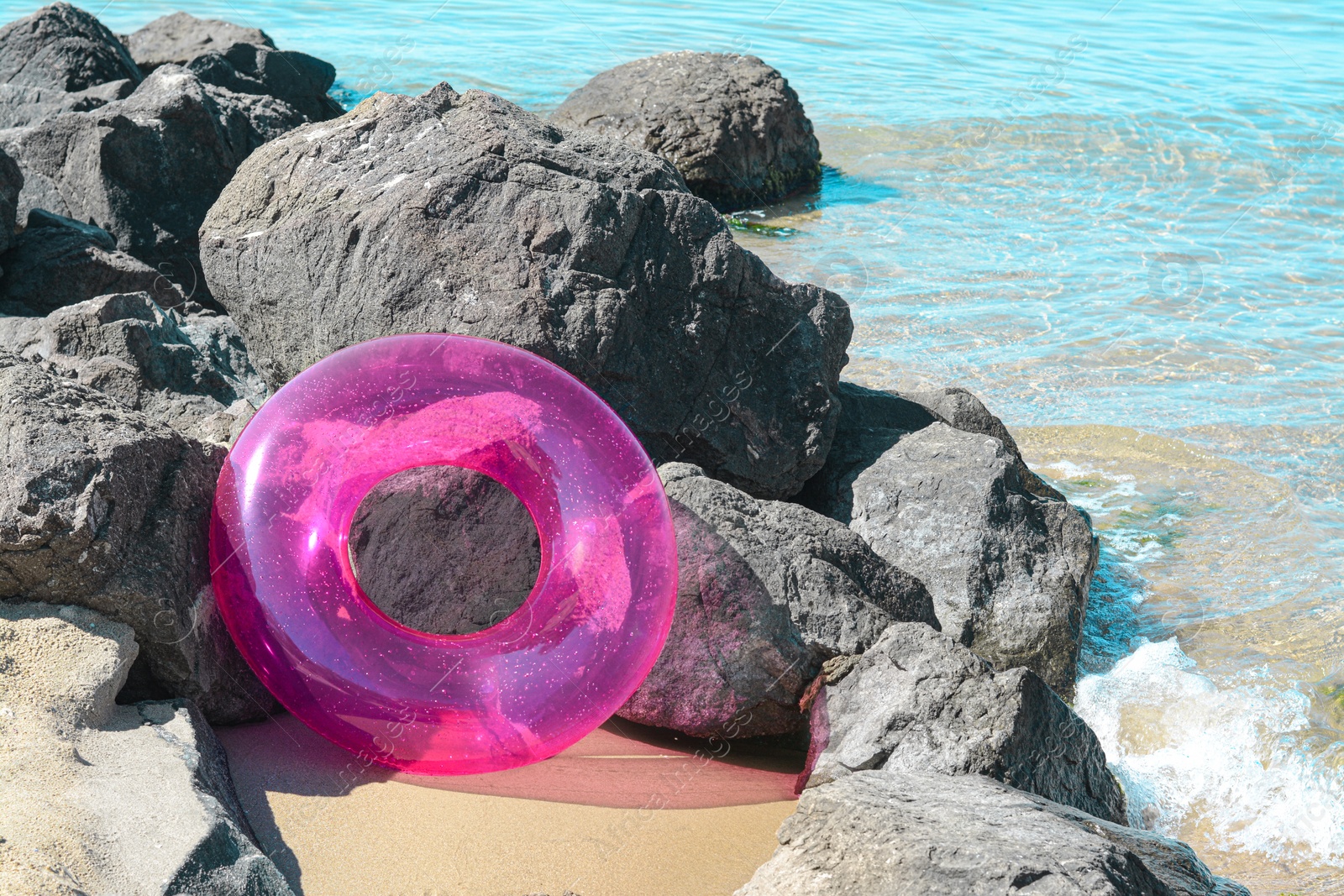 Photo of Bright inflatable ring on sandy beach near rocks