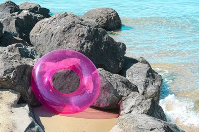 Bright inflatable ring on sandy beach near rocks