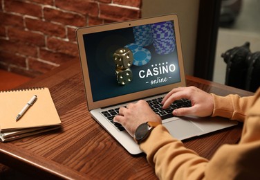 Image of Man playing poker on laptop at wooden table, closeup. Casino online