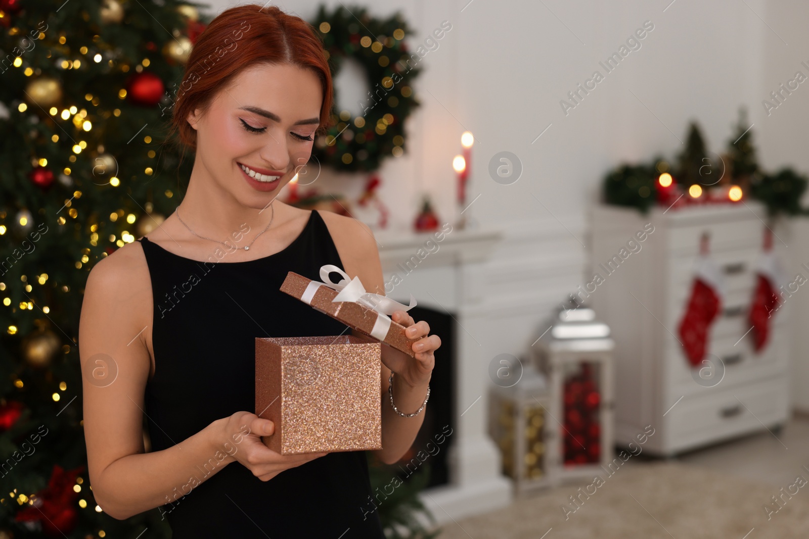Photo of Happy young woman opening gift box in room decorated for Christmas, space for text