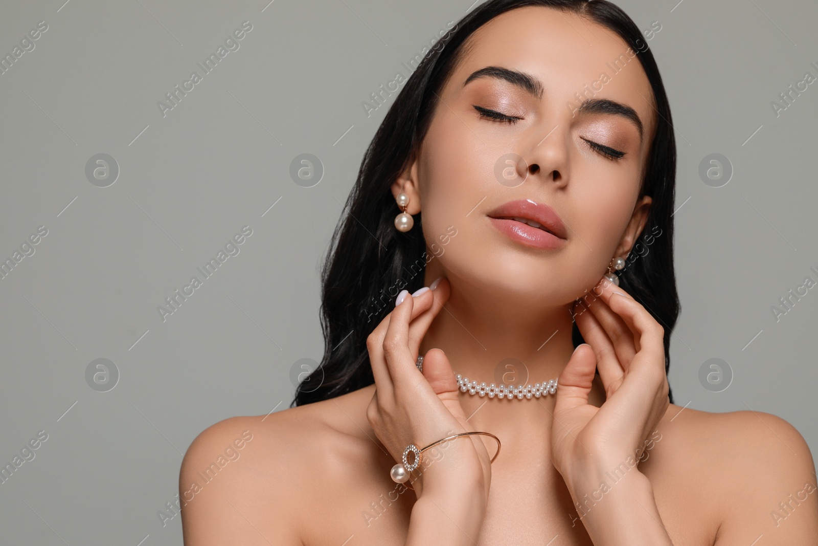 Photo of Young woman wearing elegant pearl jewelry on grey background, space for text