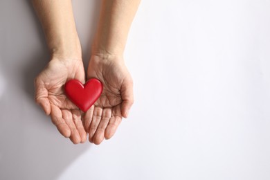 Elderly woman holding red heart in hands on white background, top view