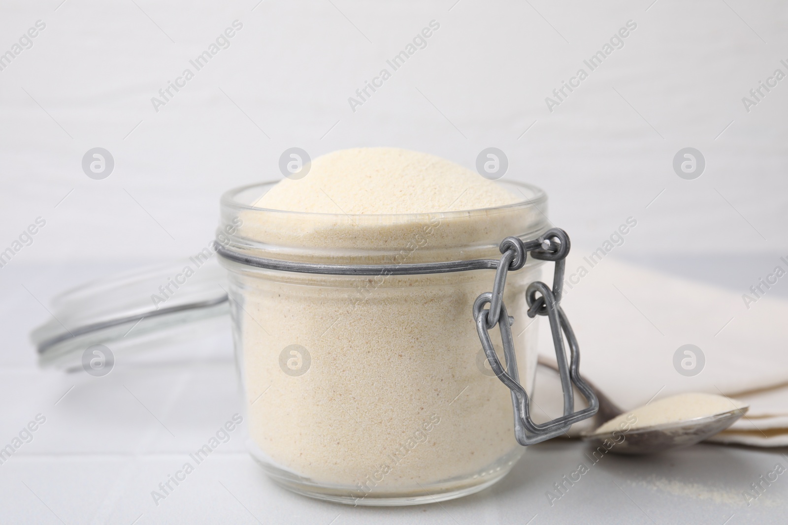 Photo of Uncooked organic semolina in jar and spoon on white tiled table, closeup