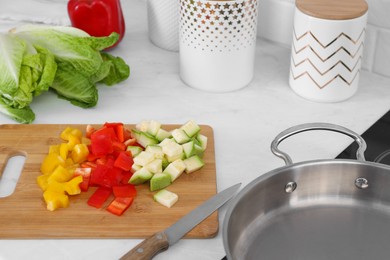 Wooden board with cut vegetables and knife near saute pan in kitchen