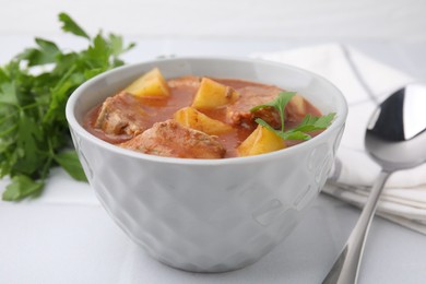 Photo of Delicious goulash in bowl on white tiled table, closeup