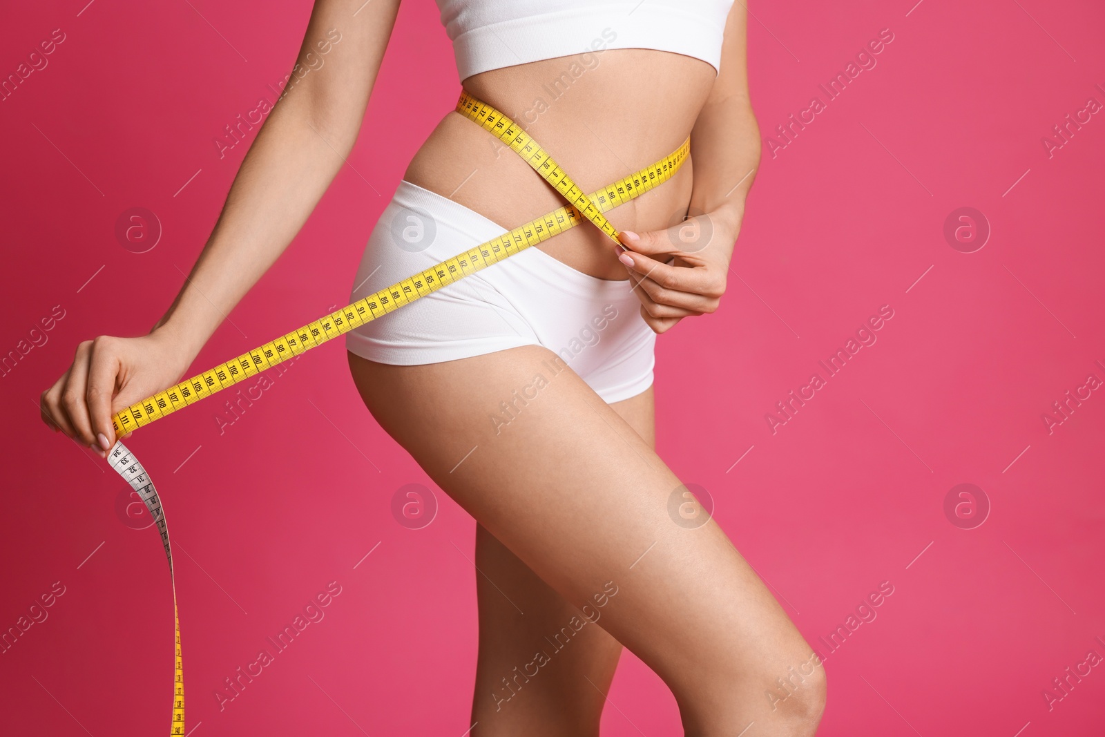 Photo of Young woman measuring waist with tape on pink background, closeup