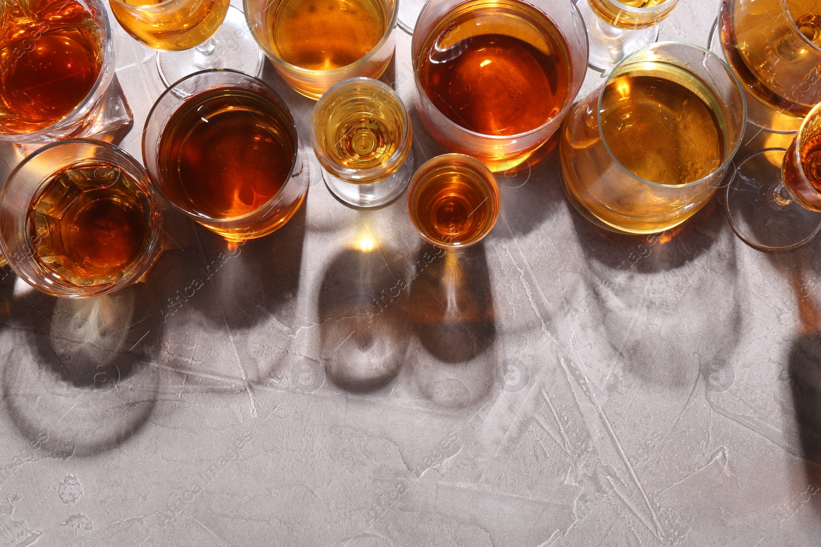 Photo of Many different liqueurs in glasses on grey textured table, flat lay. Space for text