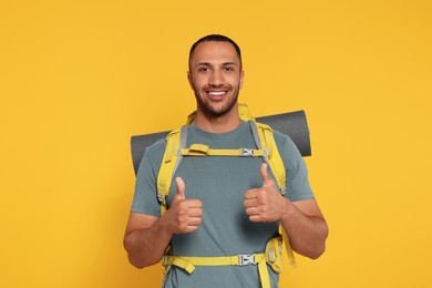 Happy tourist with backpack showing thumbs up on yellow background