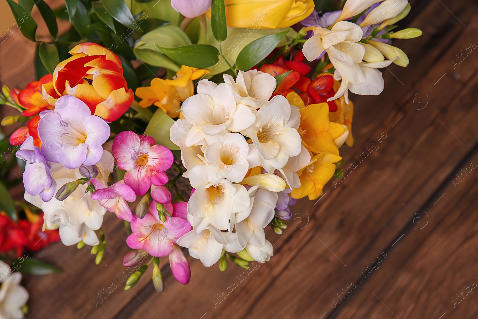 Photo of Beautiful bouquet of freesia flowers on wooden table