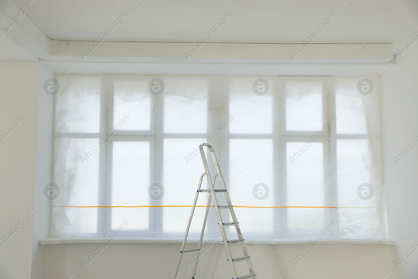Photo of Windows covered by plastic film and ladder in renovated room