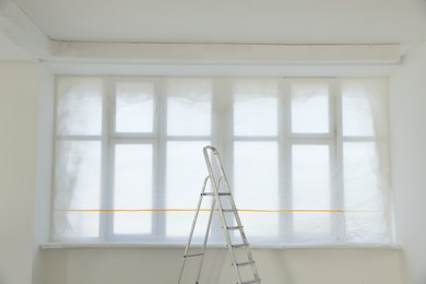 Windows covered by plastic film and ladder in renovated room