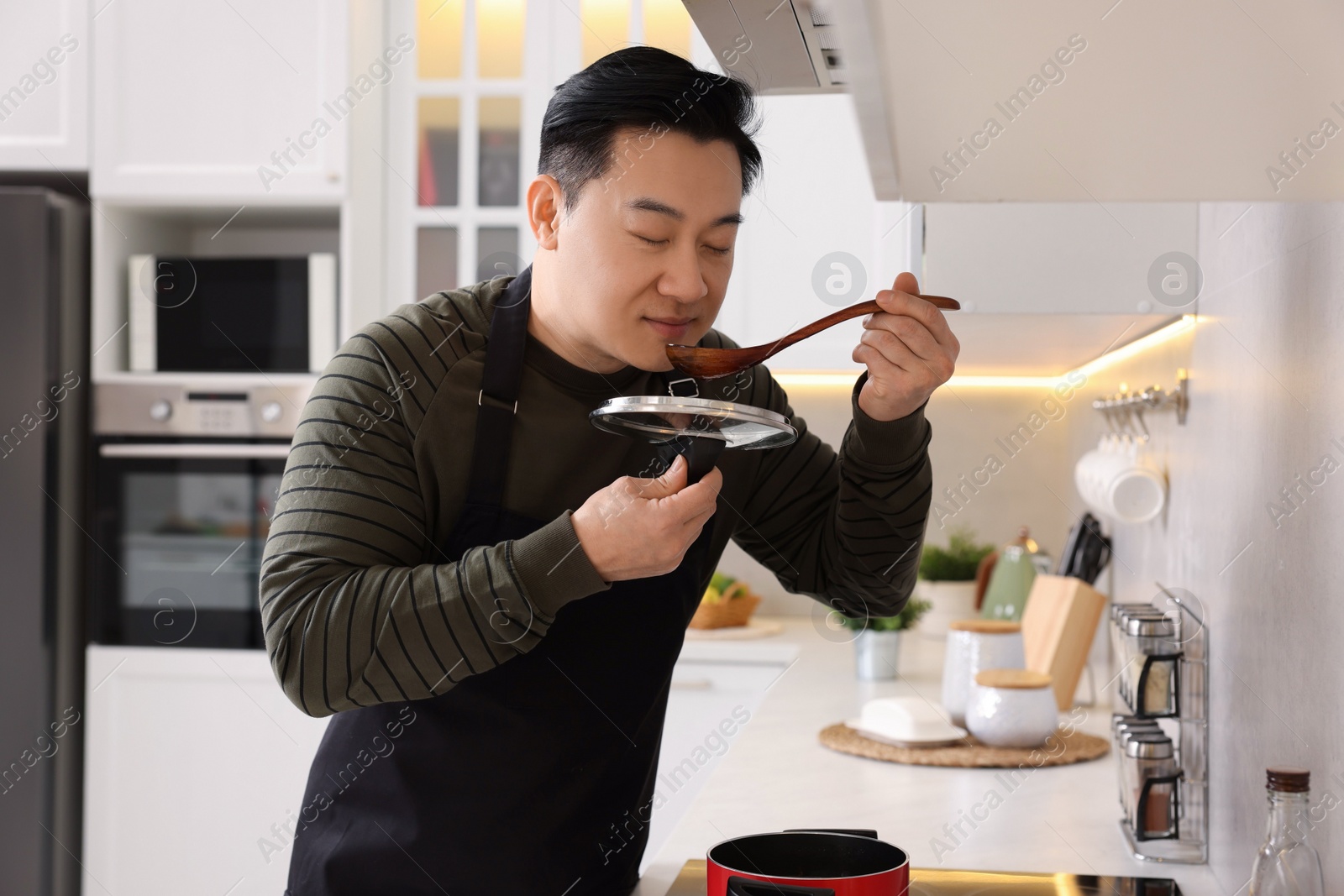 Photo of Cooking process. Man tasting dish in kitchen