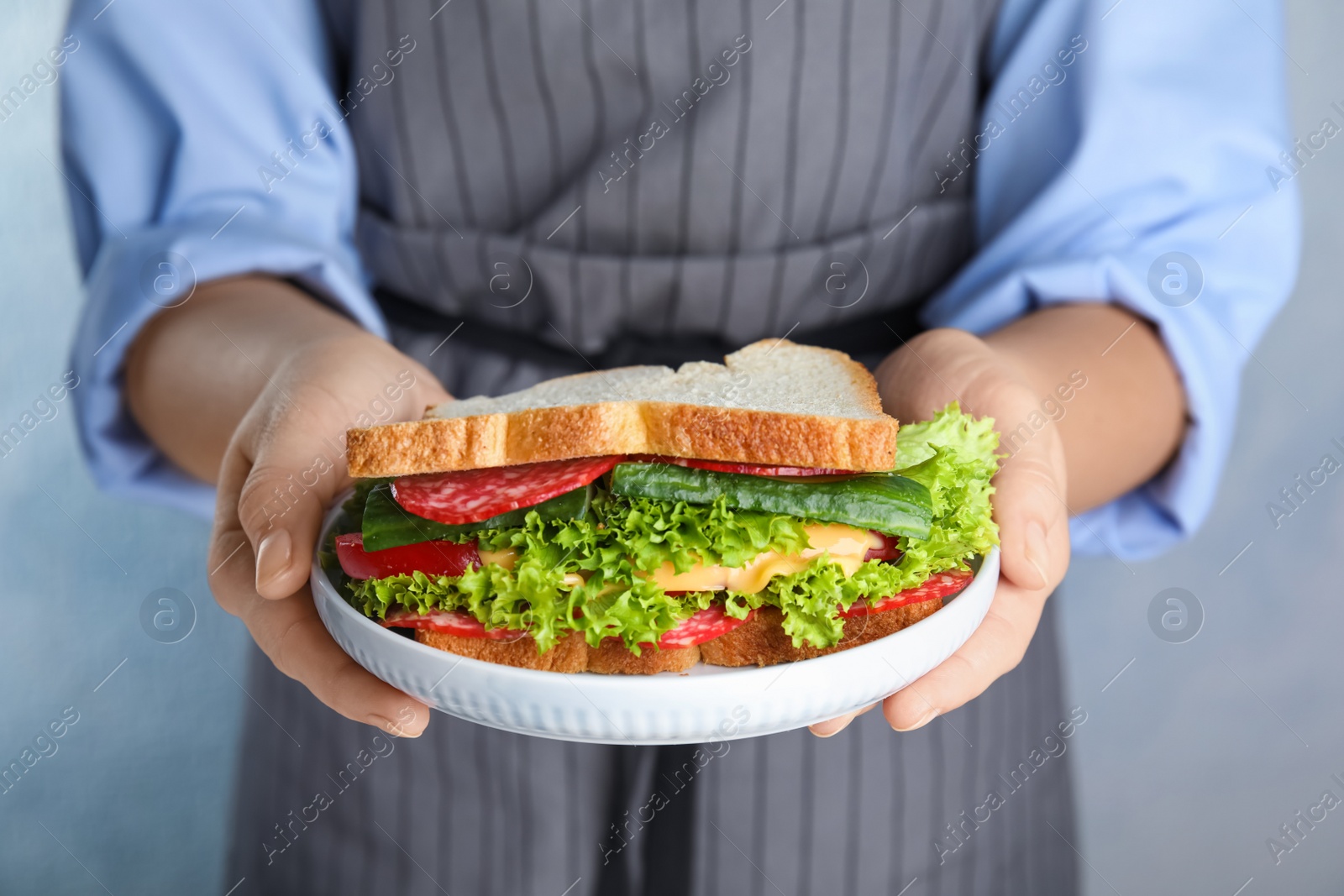 Photo of Woman holding plate with tasty sandwich on light background, closeup