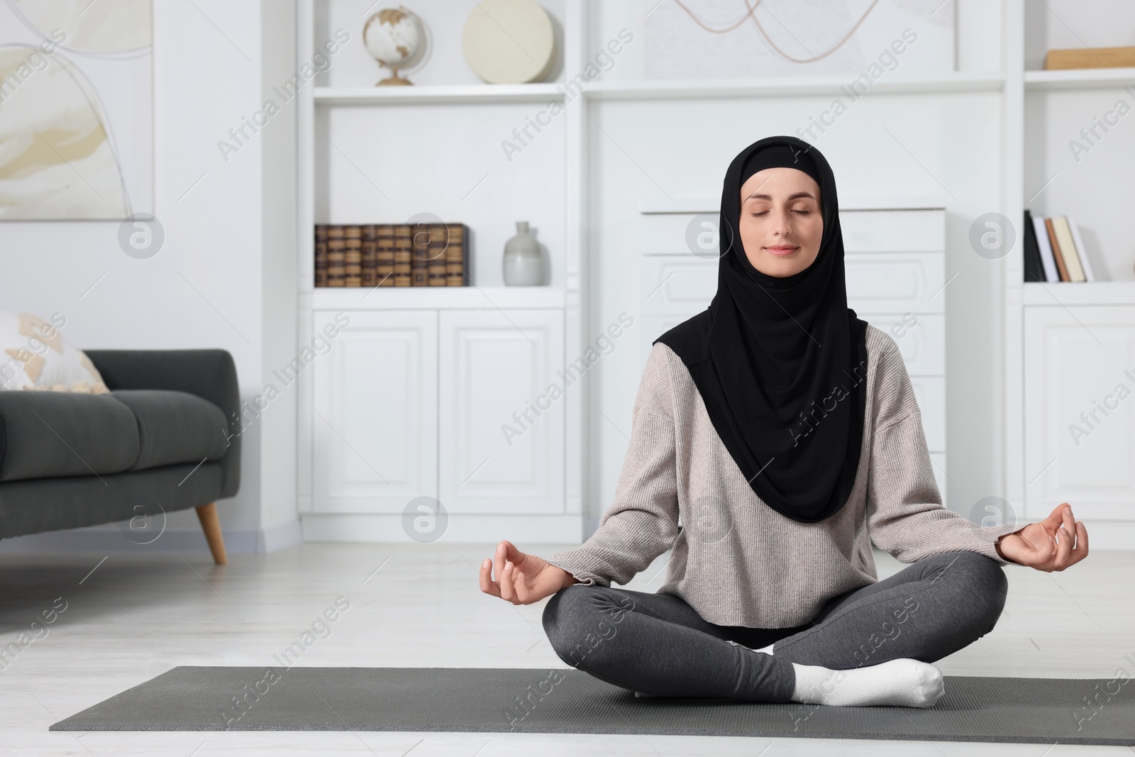 Photo of Muslim woman in hijab meditating on fitness mat at home. Space for text