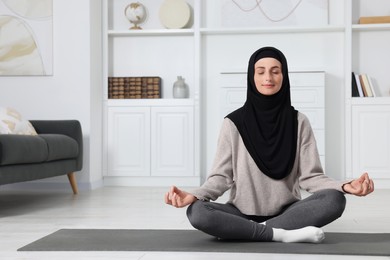 Muslim woman in hijab meditating on fitness mat at home. Space for text