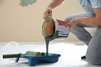 Photo of Young man pouring paint from bucket into tray indoors, closeup. Home repair