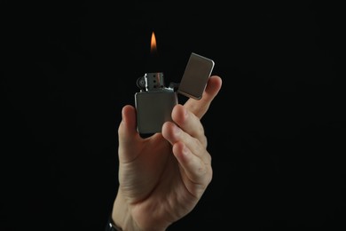 Photo of Man holding lighter with burning flame on black background, closeup