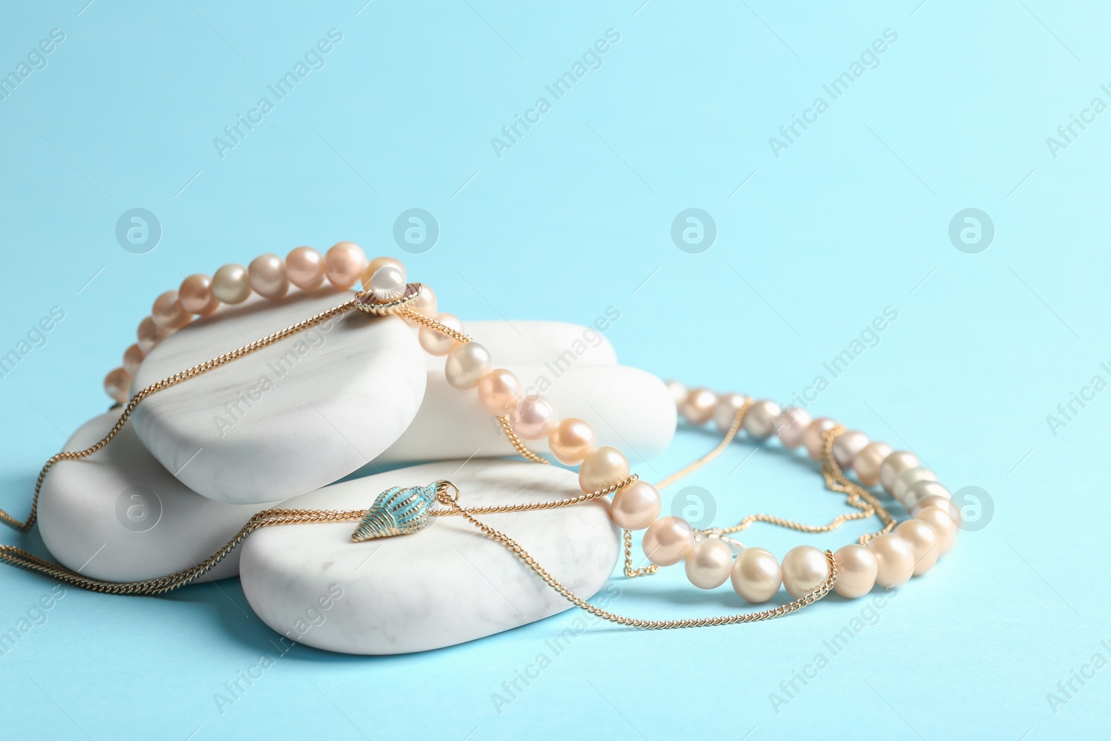 Photo of White marble stones with elegant jewelry on light blue background. Space for text